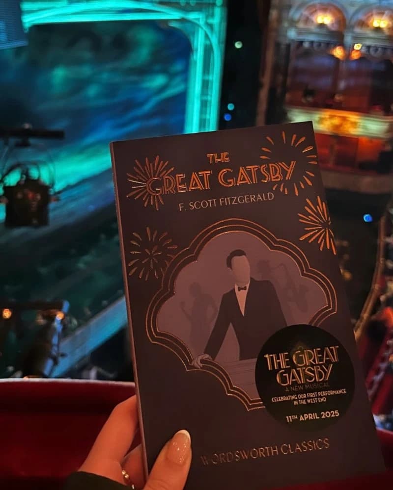 A guest holding The Great Gatsby paperback with the musical’s stage in the background.